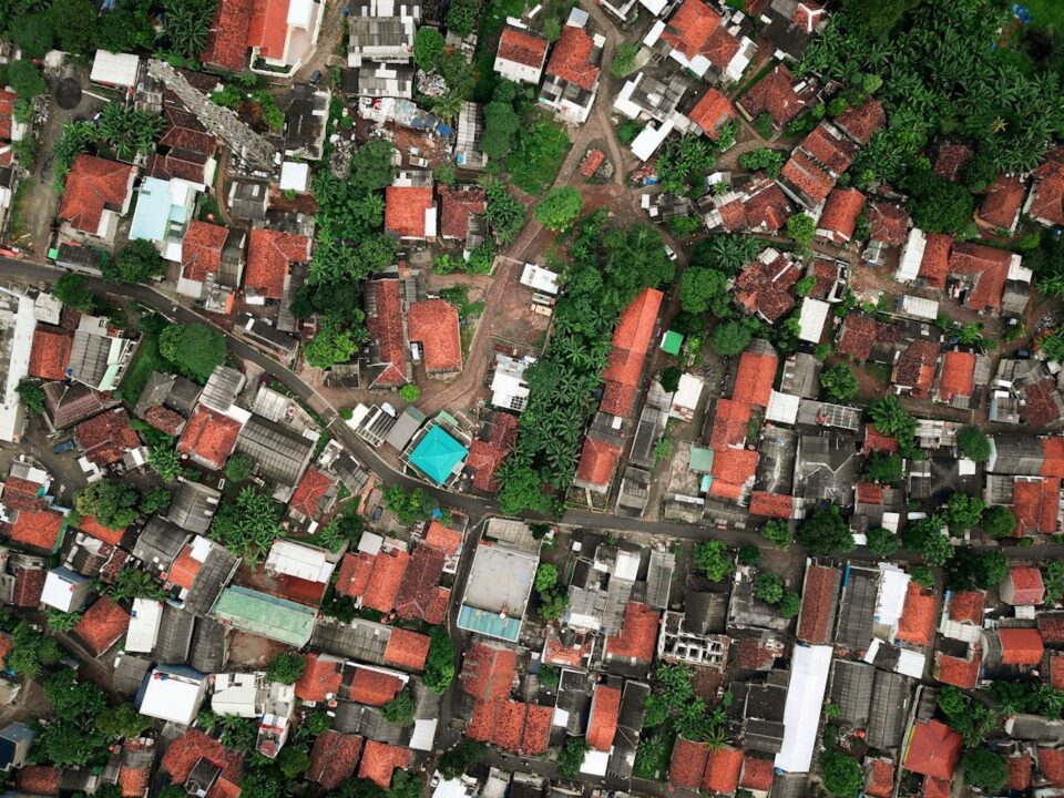 Aerial view of a densely packed residential area with red-roofed houses, narrow streets, and patches of green trees scattered throughout the neighborhood.