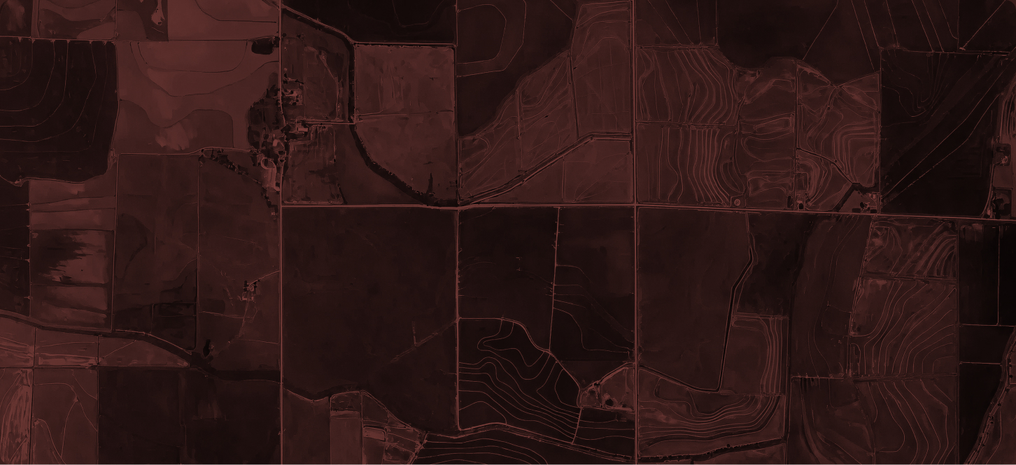 Satellite view of a dark body of water surrounded by mountainous desert terrain, with a patchwork of green and brown agricultural fields at the water's edge, under reddish lighting.
